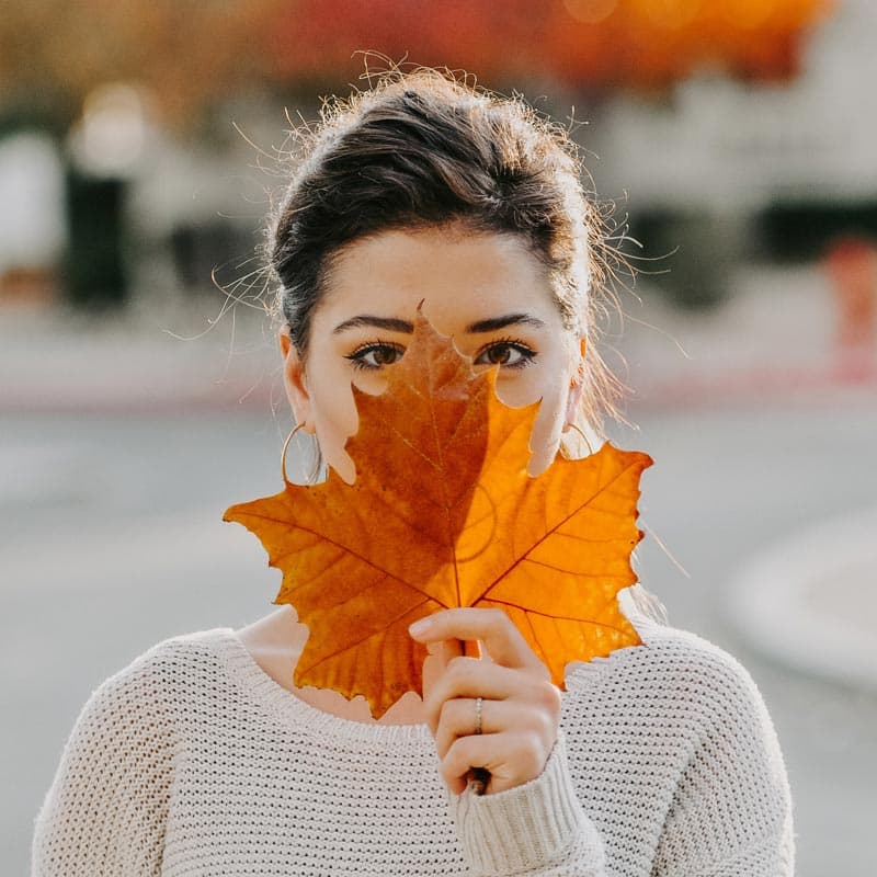 Femme tenant une feuille d'automne, symbolisant les soins de la peau pendant la saison automnale